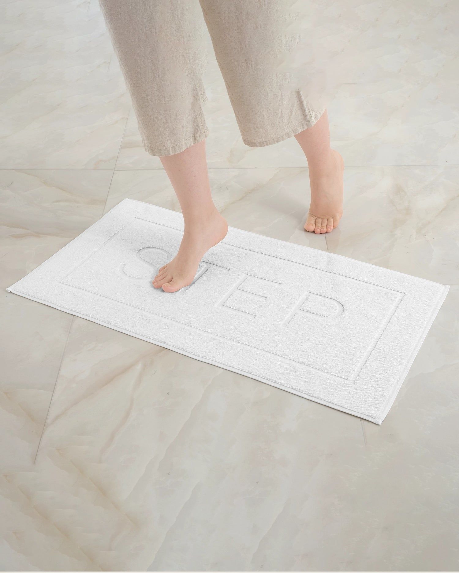 Feet stepping on a white textured bath mat on a light tiled floor