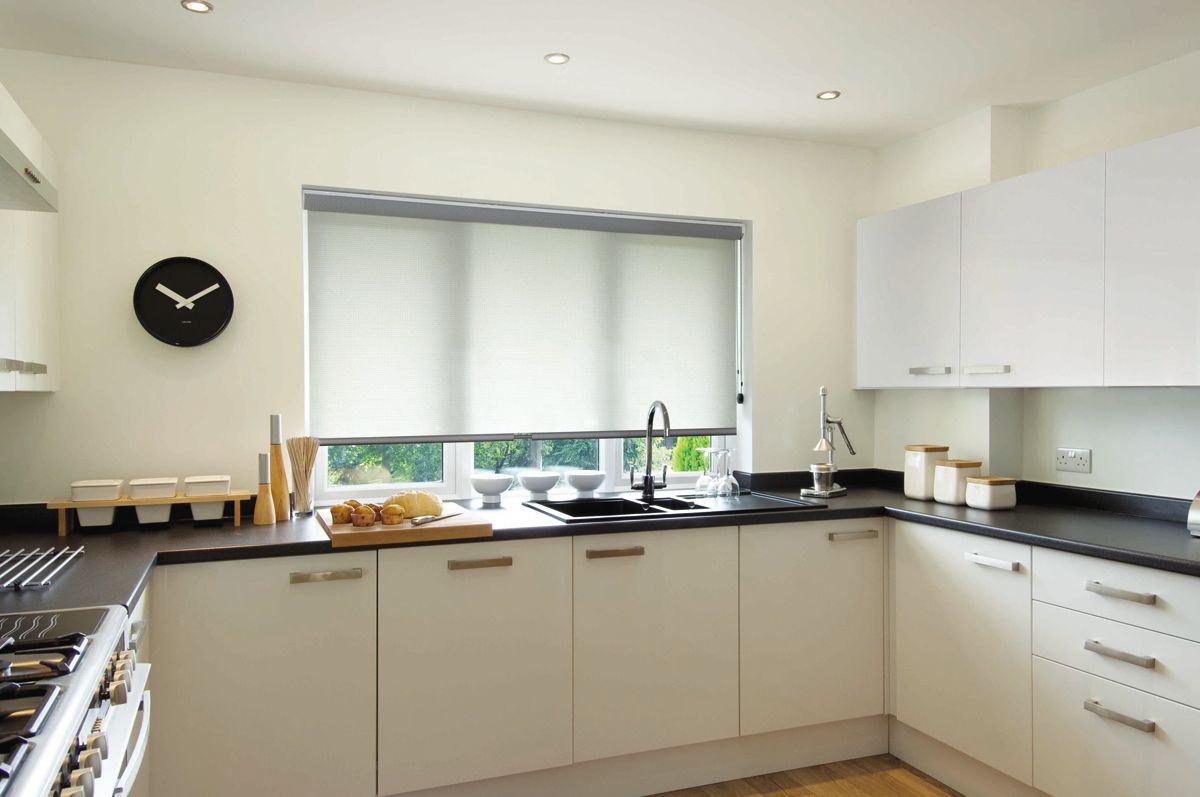 Modern white kitchen with black clock, beige cabinets, and a window over the sink