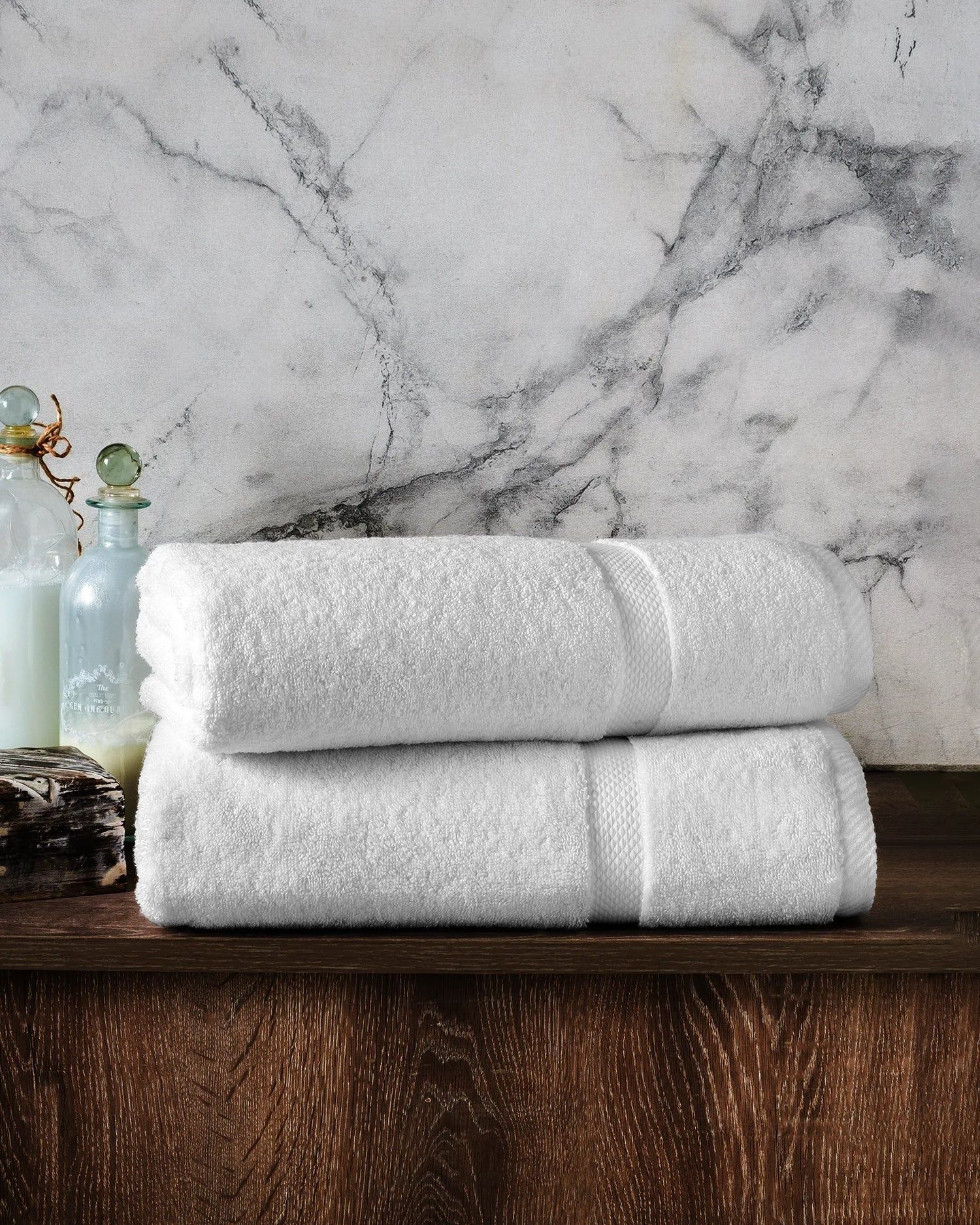 Two white folded towels stacked on a wooden surface against a marble wall