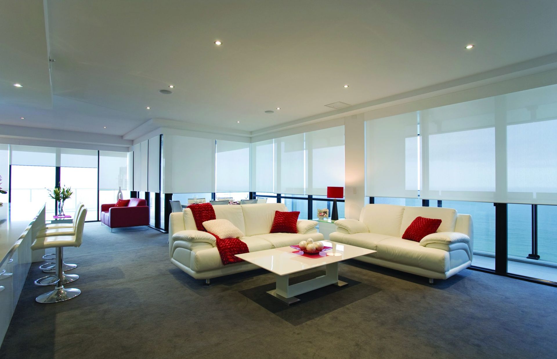 Modern living room with white sofas, red accents, and floor-to-ceiling windows overlooking water