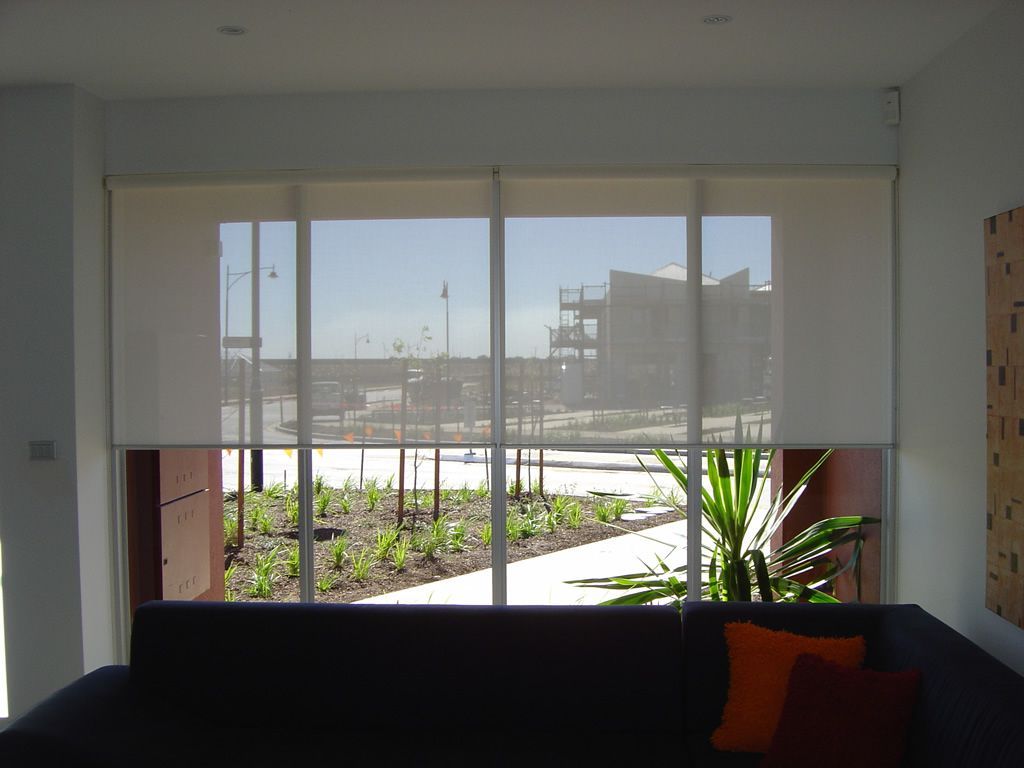 Living room with a dark sofa facing large windows overlooking a sunlit patio and buildings