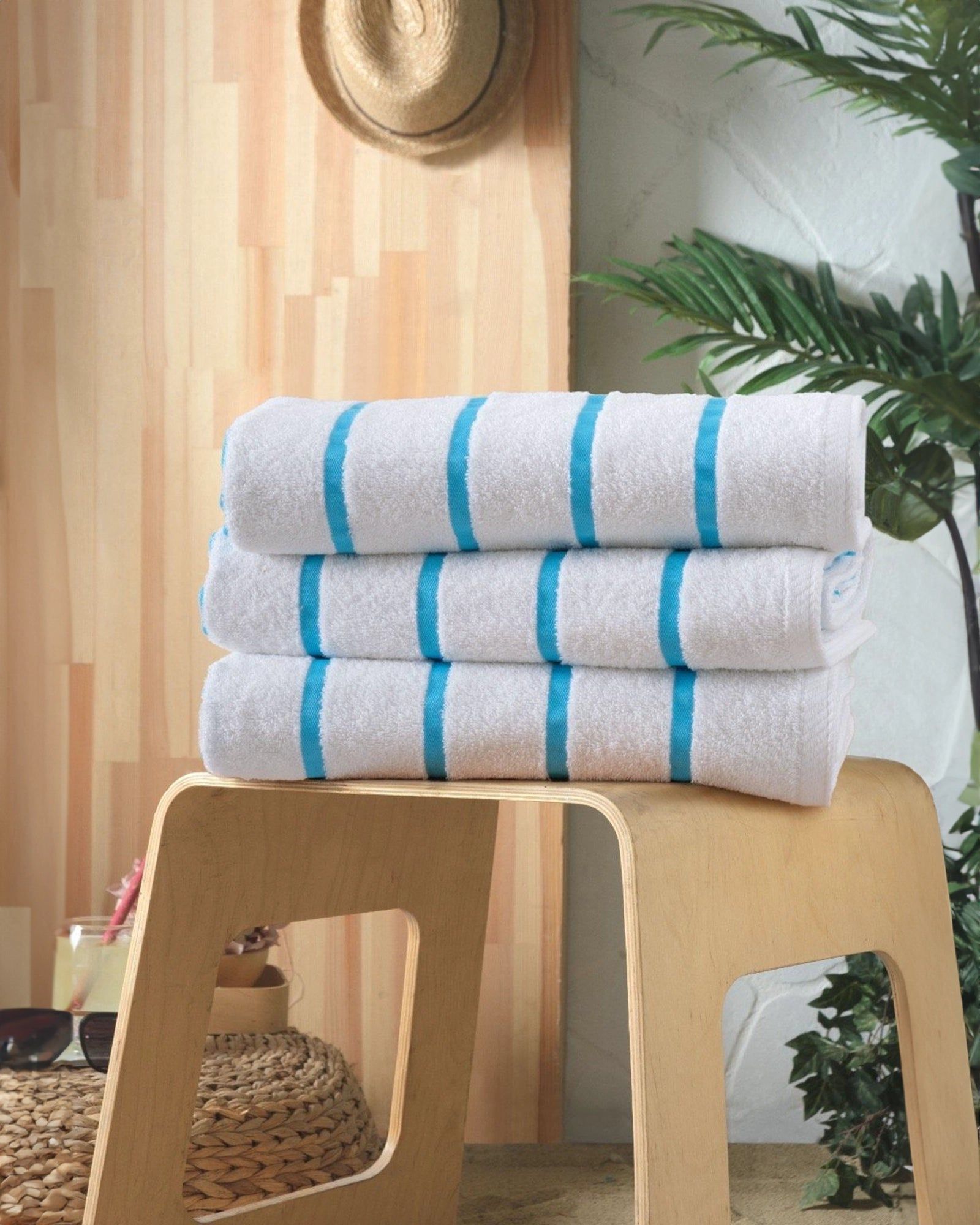 Three folded white towels with blue stripes stacked on a wooden stool in a bright room