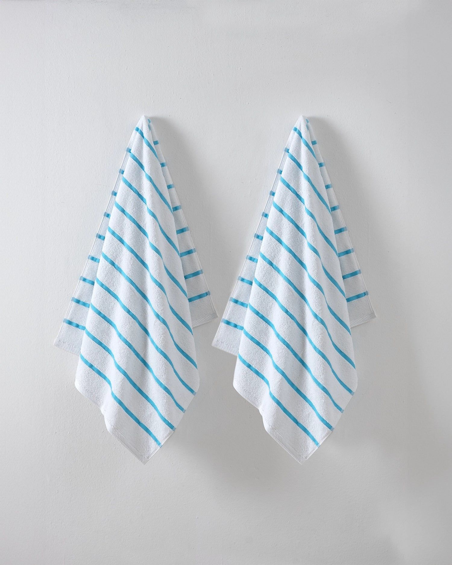 Two white cloths with blue diagonal stripes hanging side by side on a light gray wall
