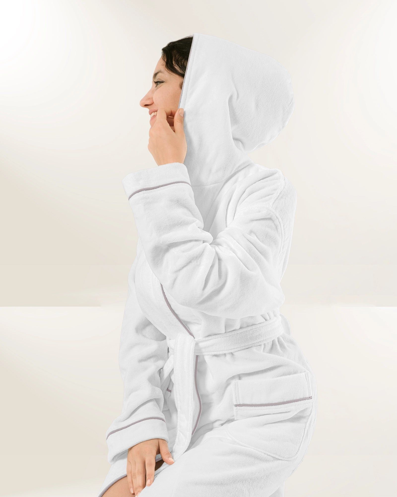 Person in a white hooded robe sitting in profile, smiling against a plain light background