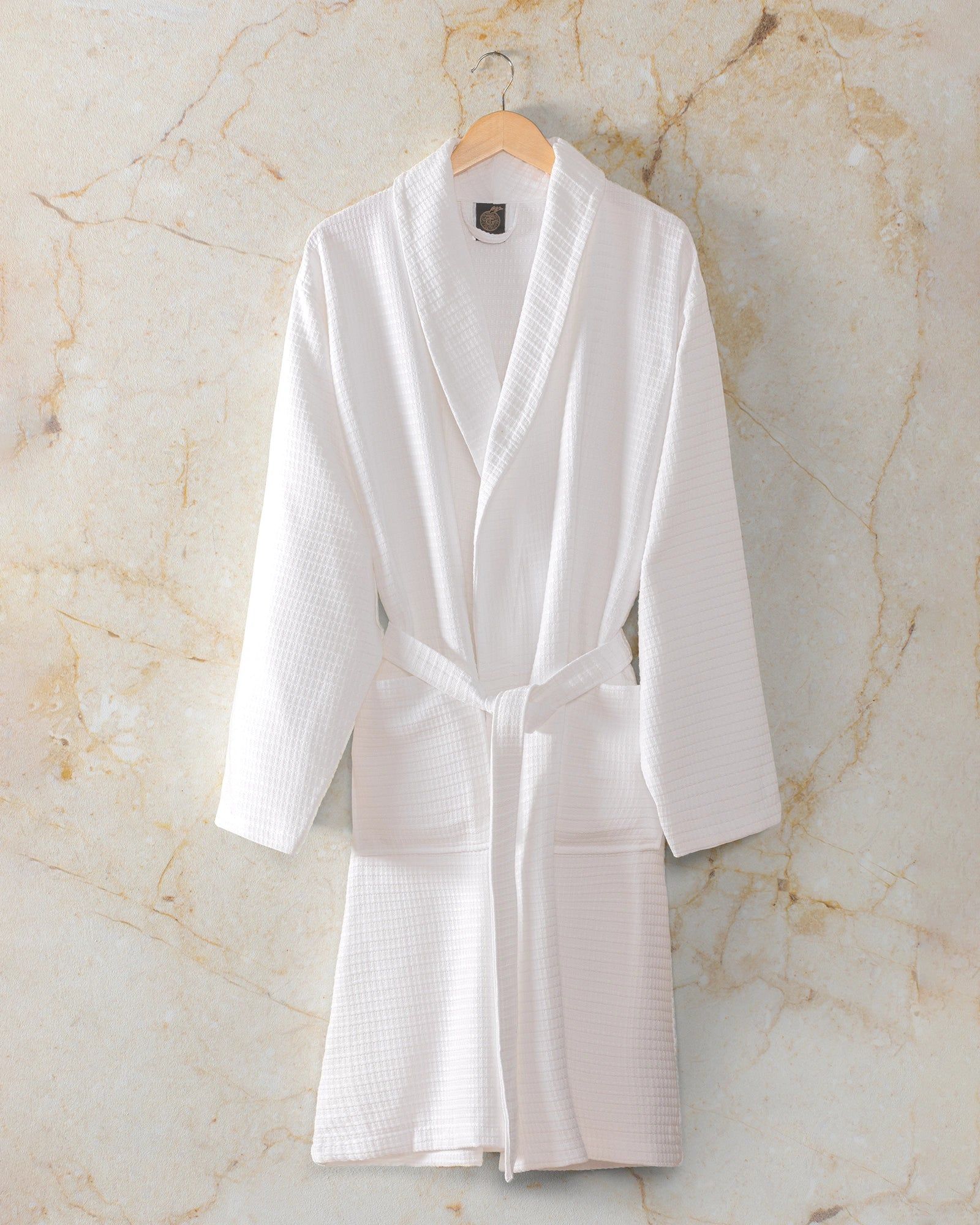 White bathrobe hanging on a wooden hanger against a light textured wall.