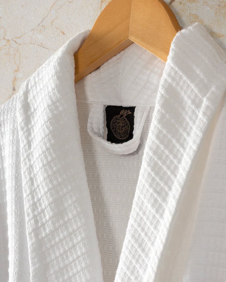 White textured robe or towel on a wooden hanger, with a black neck label visible