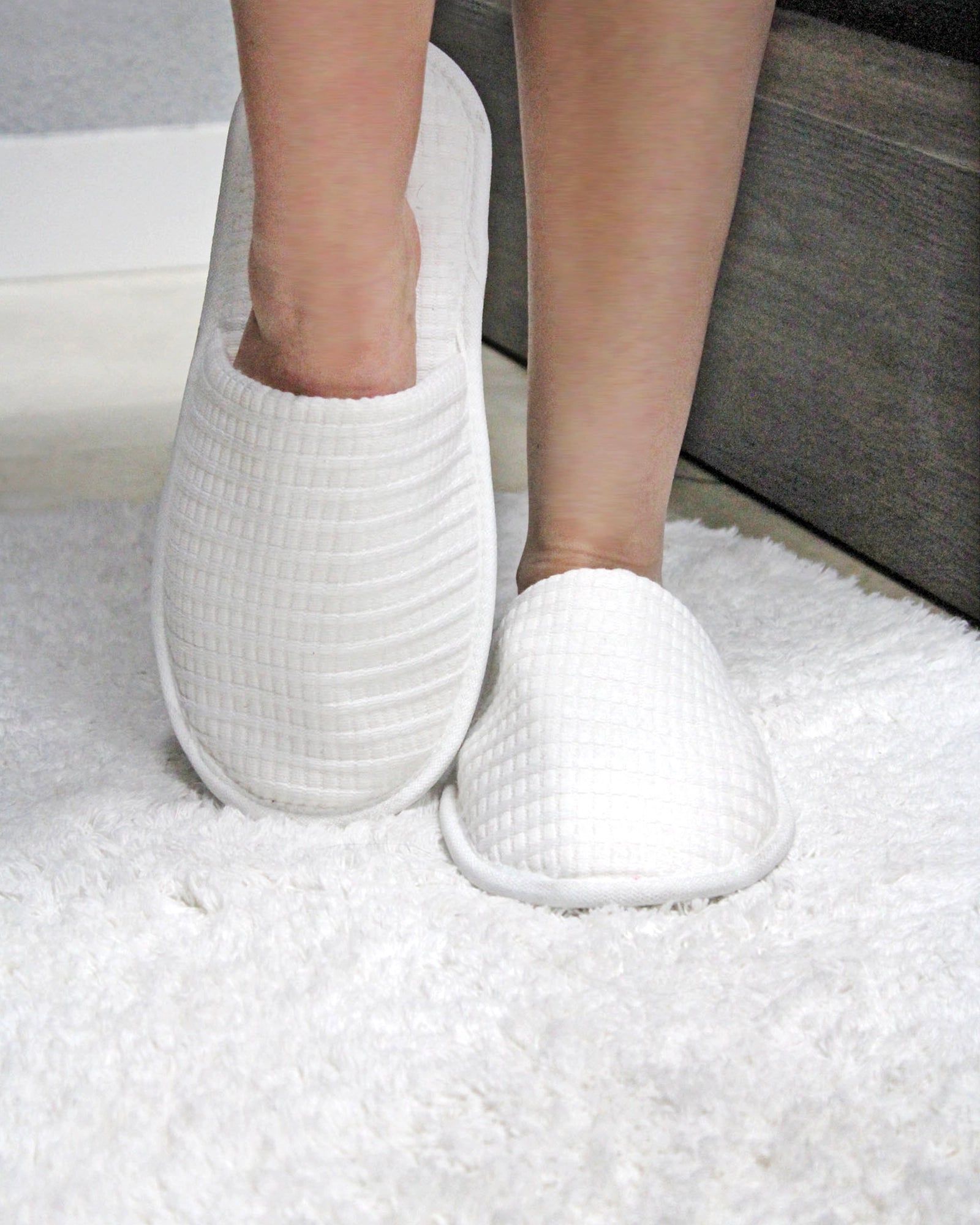 Person wearing white slippers standing on a fluffy white rug beside a gray sofa