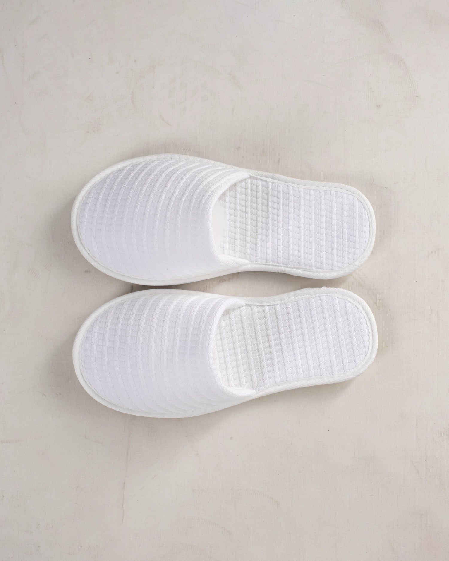 Two white textured slippers placed side by side on a light background