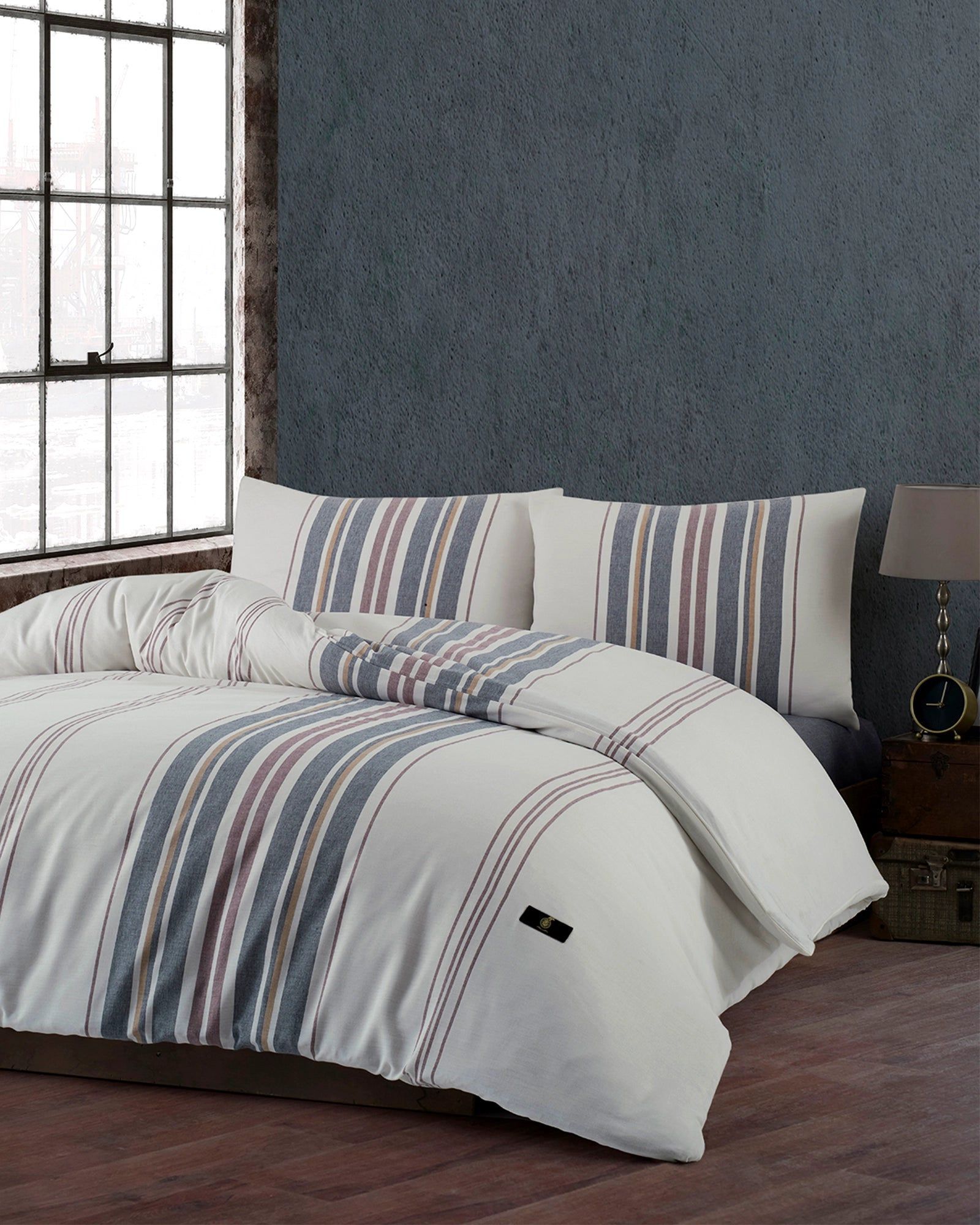 Striped white and blue bedding on a bed beside a window in a cozy bedroom