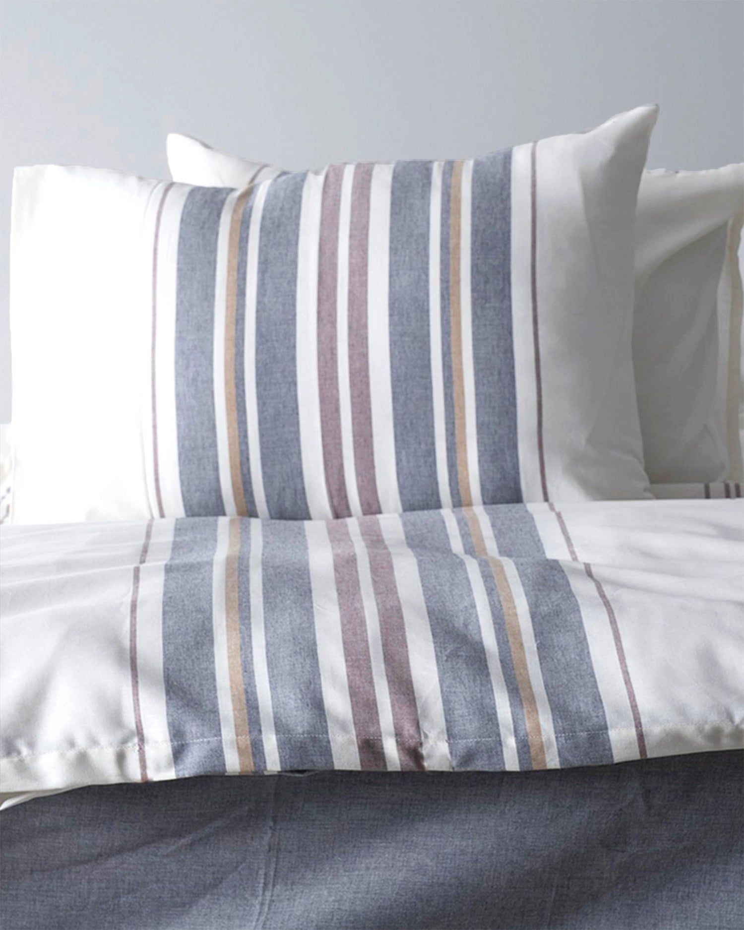 Striped blue, gray, and white bedding with pillows on a neatly made bed.