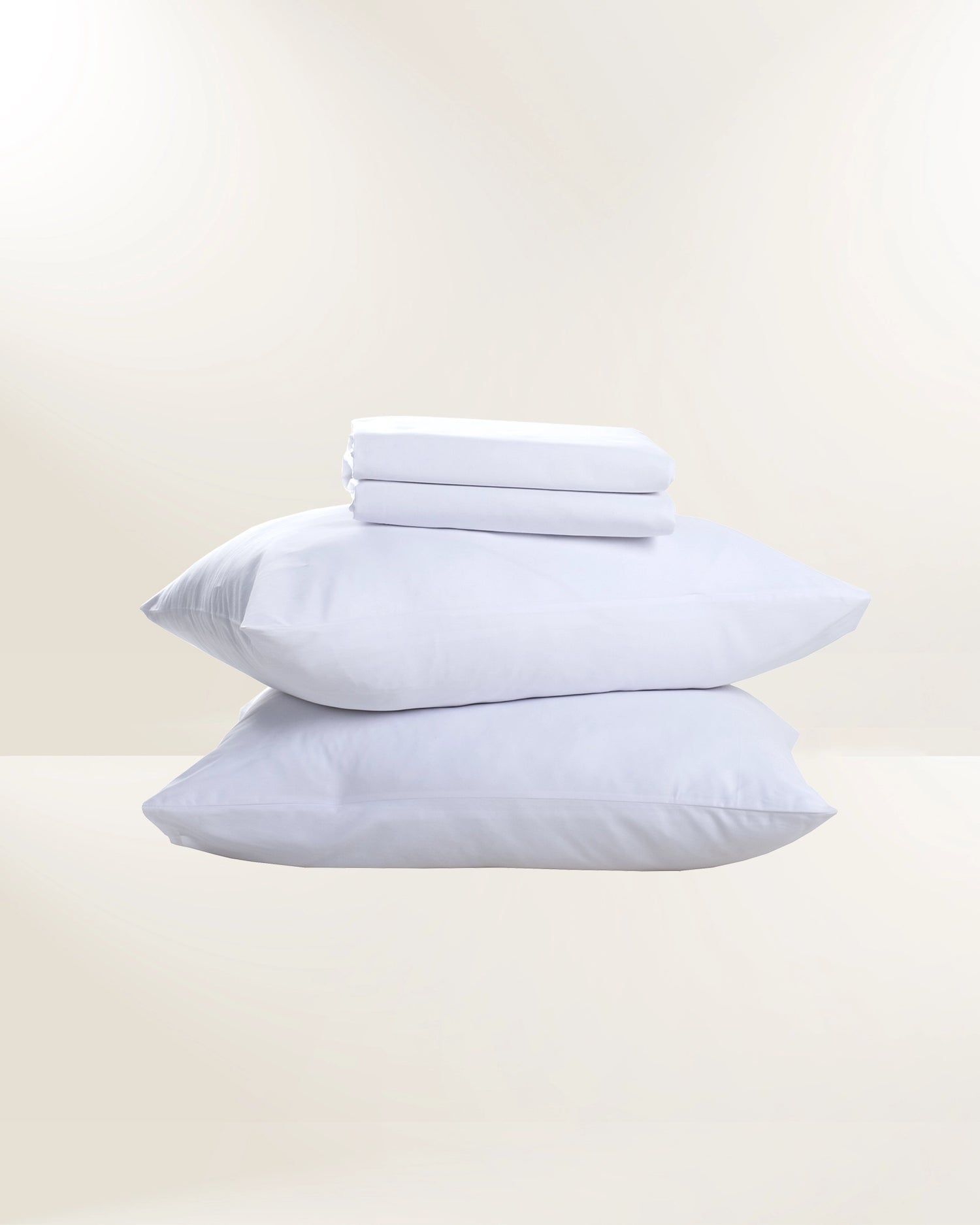 Stacked white pillows and folded towels on a light beige background