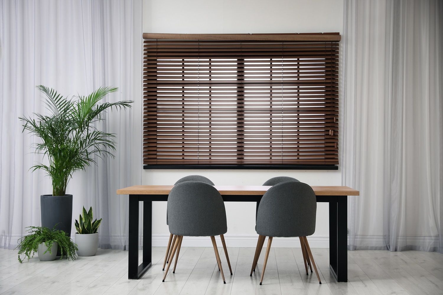 Minimal dining setup with a wooden table, two gray chairs, a potted plant, and a window with blinds