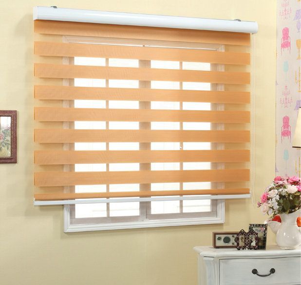 Tan wood horizontal blinds covering a window in a bright room with flowers on a nearby dresser
