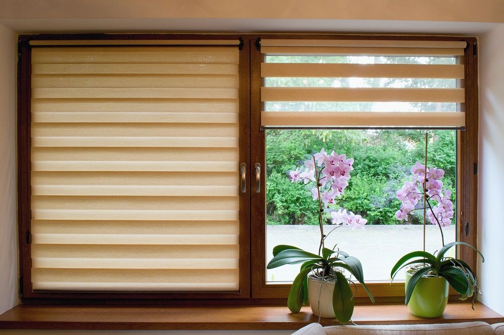 Wooden window with beige blinds and two potted orchids overlooking a blooming garden