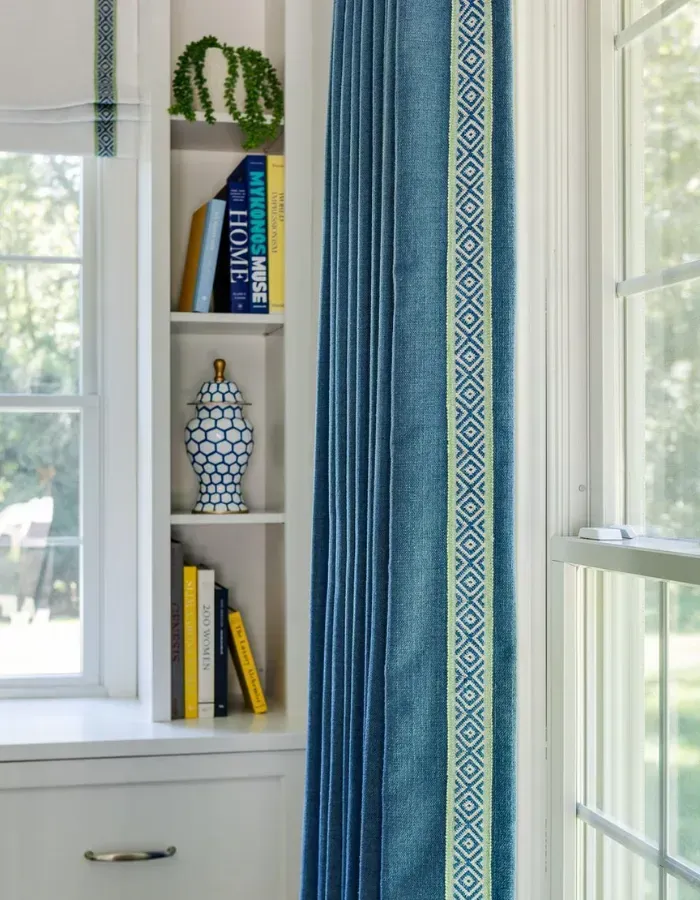 Blue patterned curtain beside a window and white shelf with books and a decorative vase
