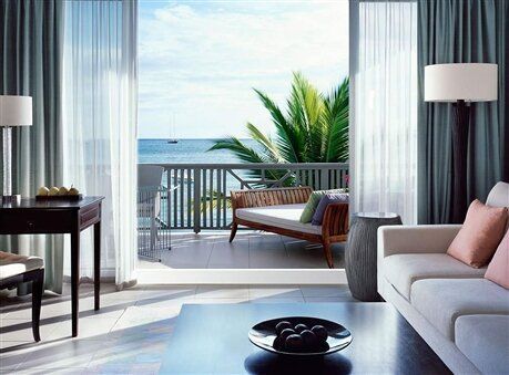Modern living room with balcony ocean view, gray sofa, and sheer curtains framing tropical greenery