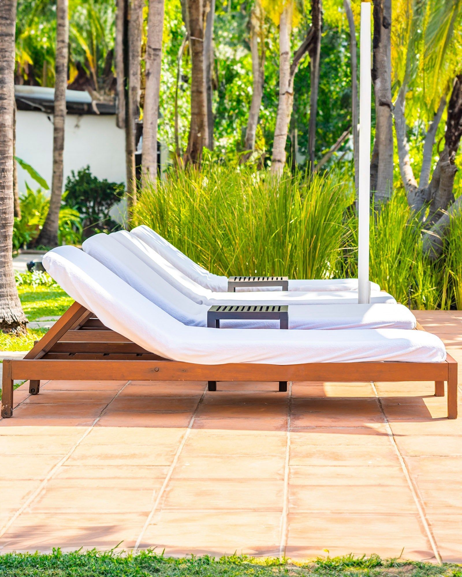 White lounge chair with striped cushions on a wooden deck beside a pool, surrounded by tropical greenery.