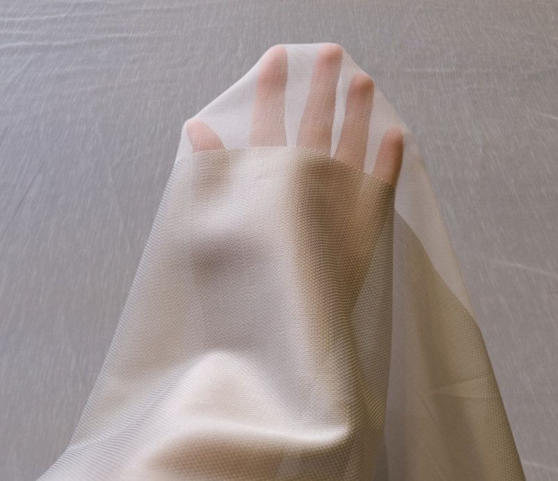 Hand under sheer beige fabric, with fingers visible through the translucent material.