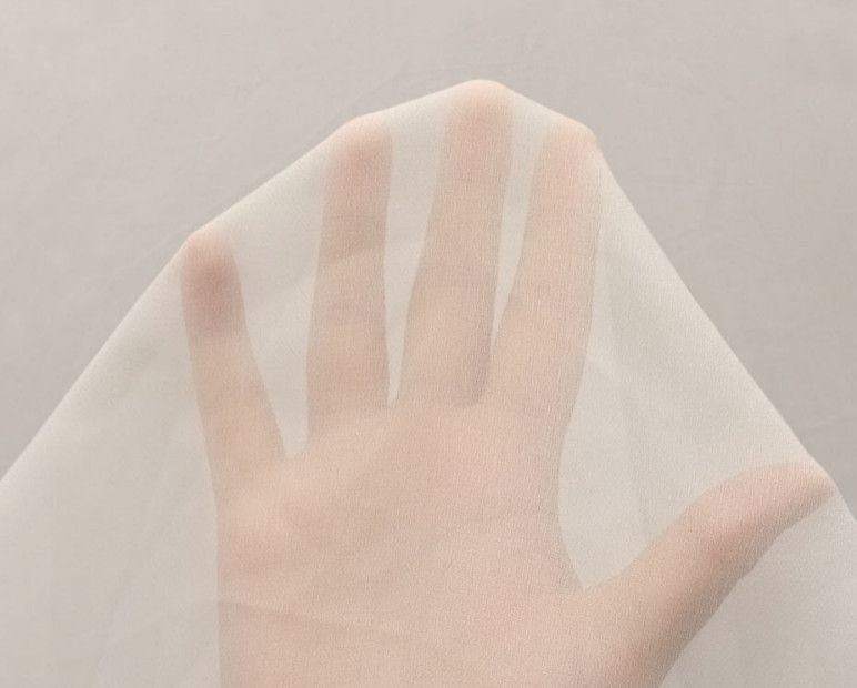 A hand gently pressing against a sheer white fabric over a beige background