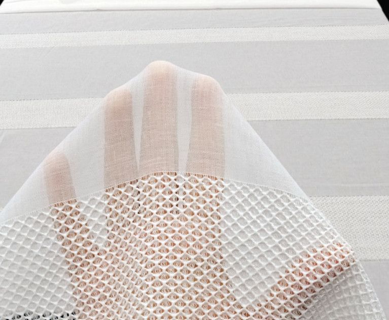 White mesh fabric draped over a pale peach hand against a light gray background