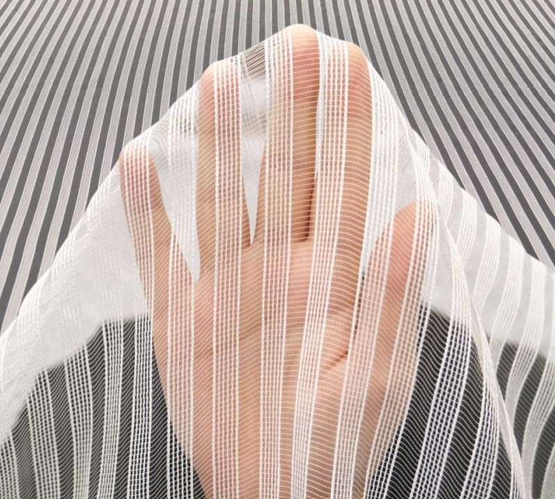 Hands holding sheer white striped fabric over a gray textured surface