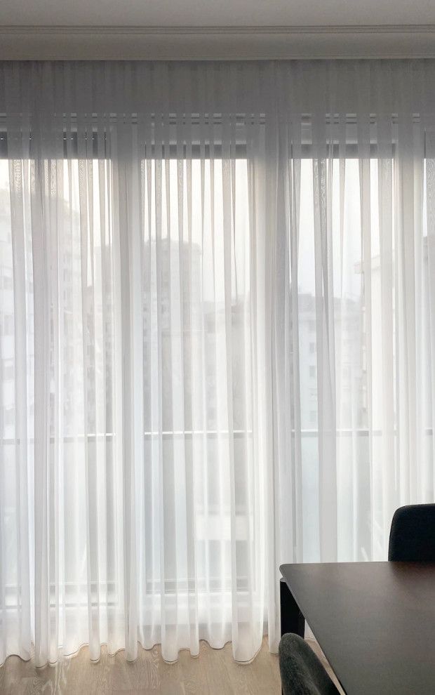Sheer white curtains over a bright window with a table edge in the foreground