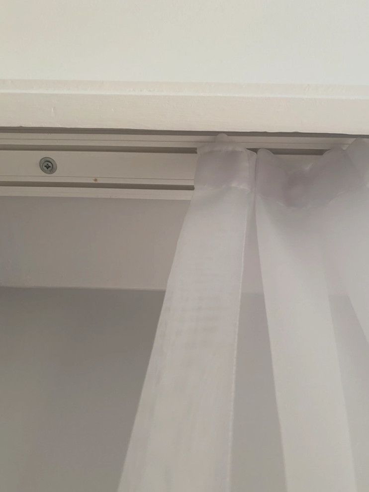 White curtain hanging from a ceiling-mounted track beside a gray wall and white ceiling trim