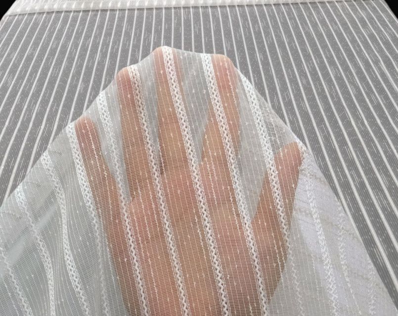 Hand under a white sheer mesh fabric with beige striped pattern on a textured surface