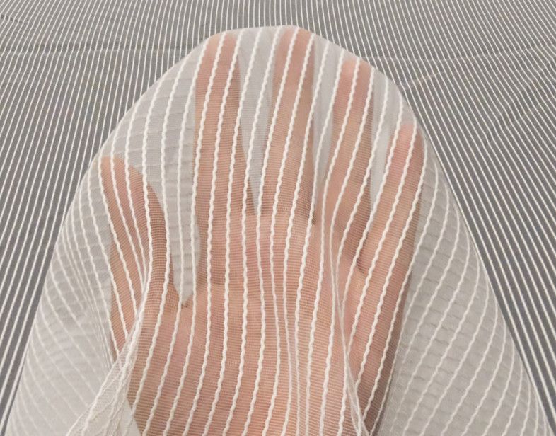 A hand seen through a sheer white striped mesh fabric on a gray background