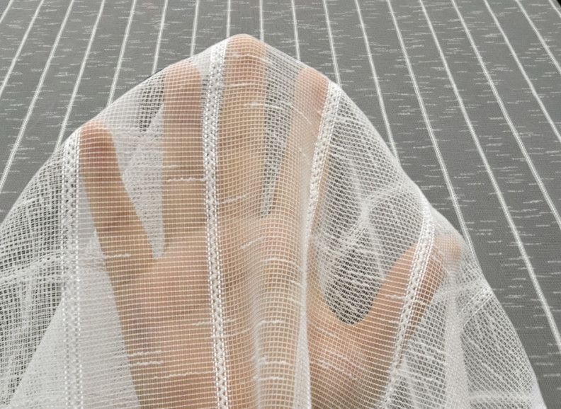 Hands behind sheer white mesh fabric against a gray striped background