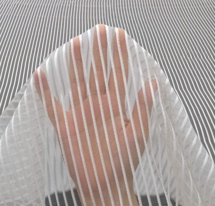 Hand under a sheer white striped fabric curtain, with a gray striped background.