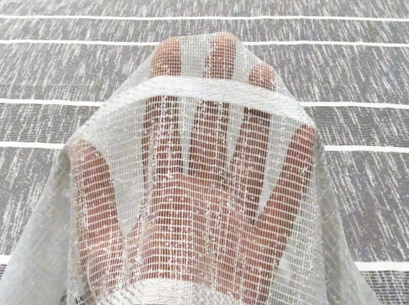 A hand under white mesh netting on a gray wooden surface