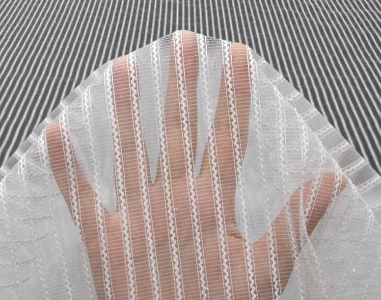 Hand with white lace glove resting on a striped gray fabric background