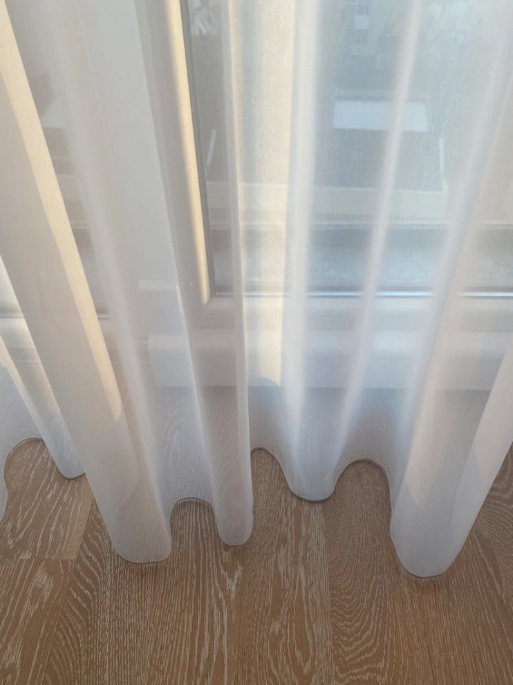 Sheer white curtains over a window above a wood floor