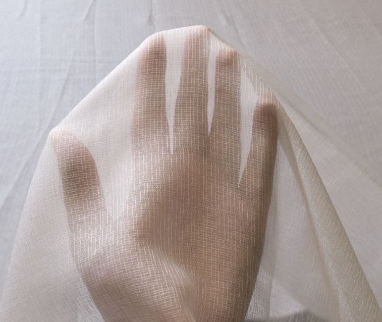 Hand pressing against sheer white fabric over a white background