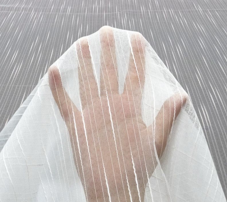 Hand beneath sheer white fabric with vertical stripes, fingers splayed against a textured gray background