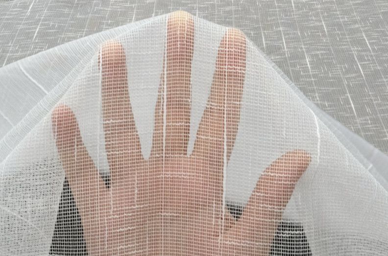 Hand beneath white mesh fabric on a gray surface