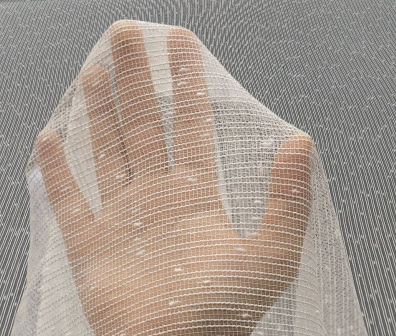 Hand pressing against a sheer white mesh fabric against a gray background