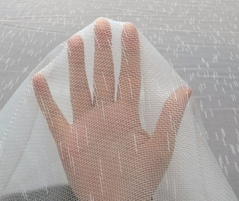 A hand seen through sheer white fabric with subtle pink stripes and a gray textured background