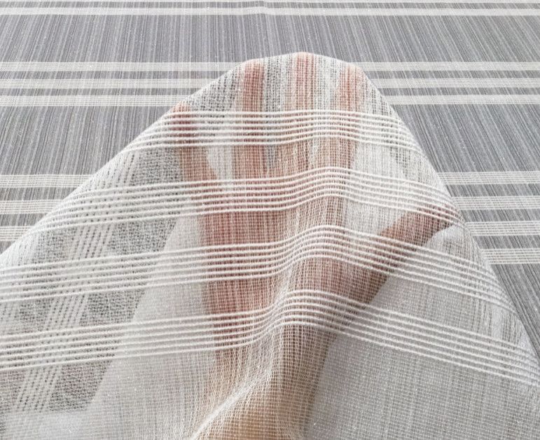 Person partially covered by a sheer white mesh fabric against a neutral striped background