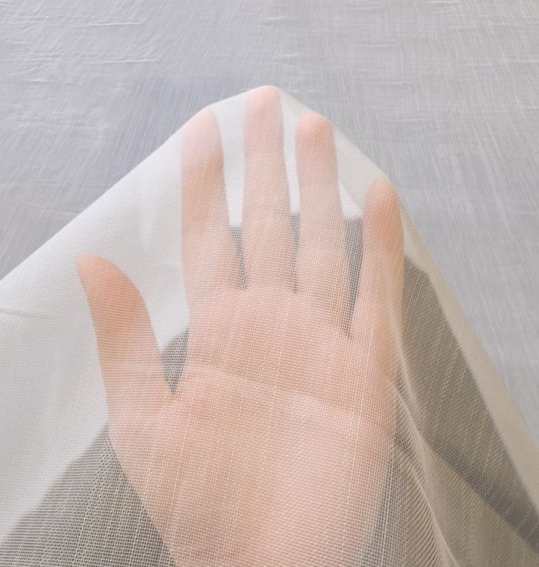 Hand resting under a sheer white mesh fabric over a light surface.