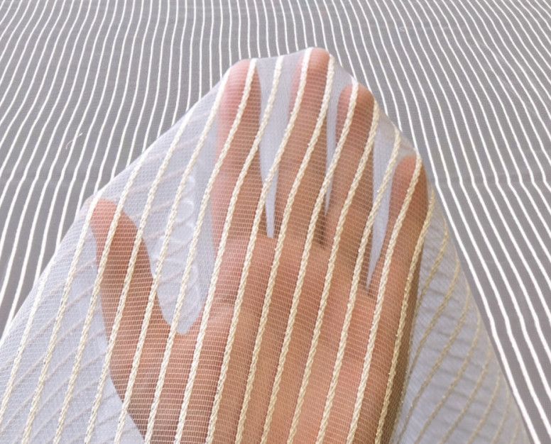A hand under a sheer striped fabric, creating a textured pink and white pattern