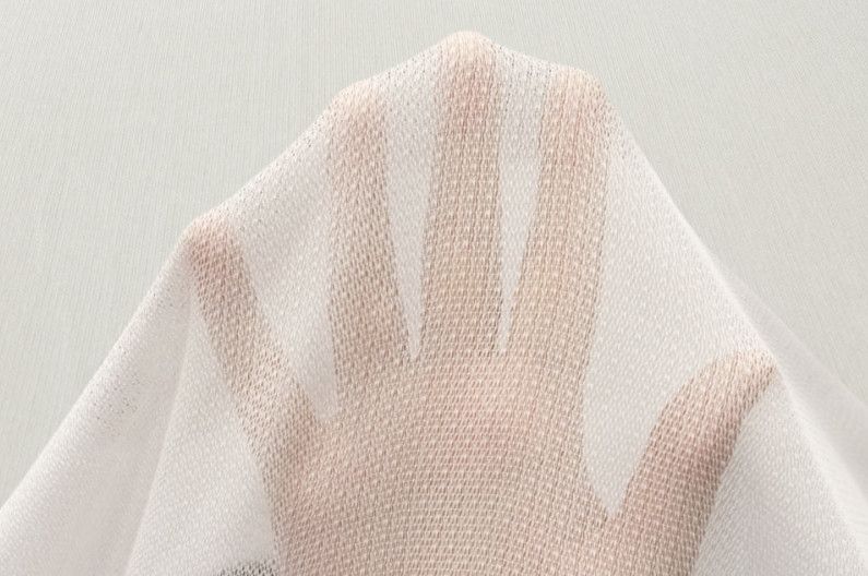 Hand pressing against a sheer white fabric veil against a light background