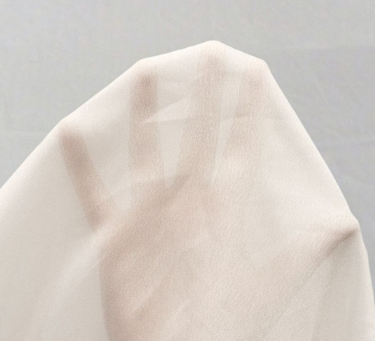 Close-up of a beige textured fabric draped into soft folds against a light gray background