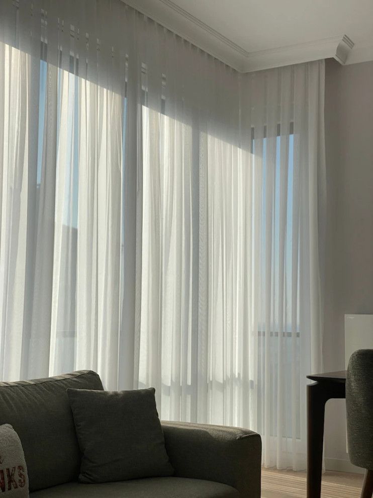 Bright living room with sheer curtains, a gray sofa, and a large window with soft daylight