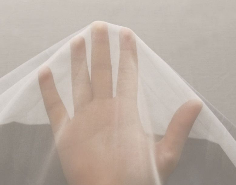 Hand beneath a sheer white fabric against a light background