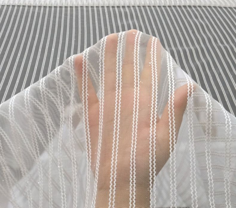 Person behind a sheer white curtain with hand raised over their face, against a gray striped background