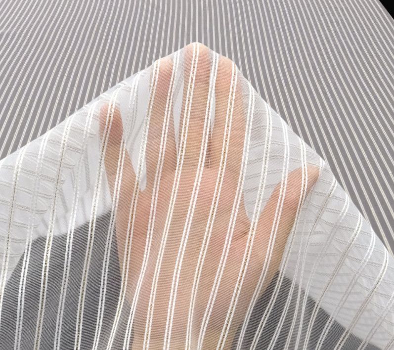 Hand raised behind a sheer white striped curtain, with a gray textured background