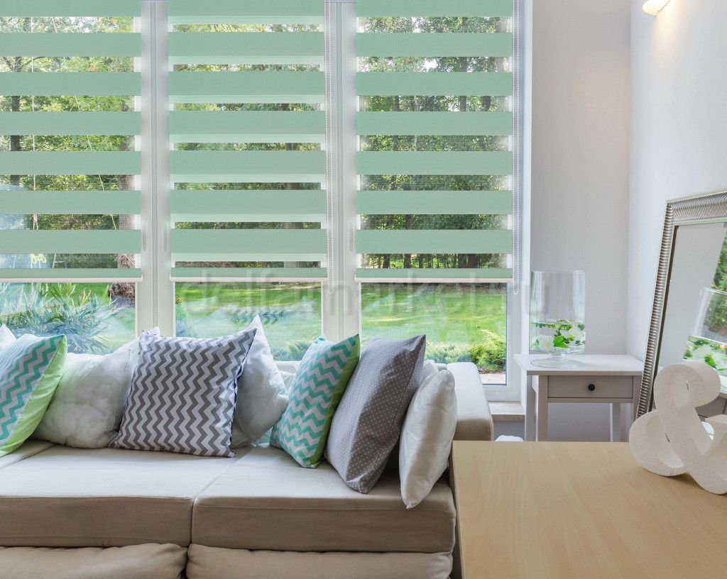 Bright living room with a beige sofa, patterned pillows, white shutters, and a small table by the window.