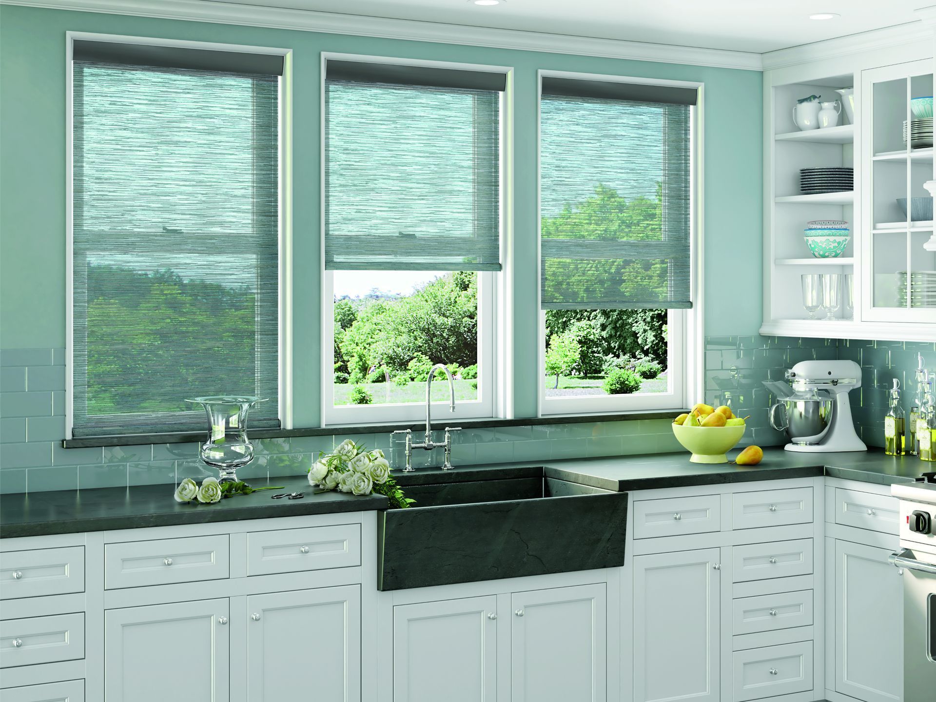 Bright mint kitchen with three windows, dark sink, white cabinets, and fruit on the counter.